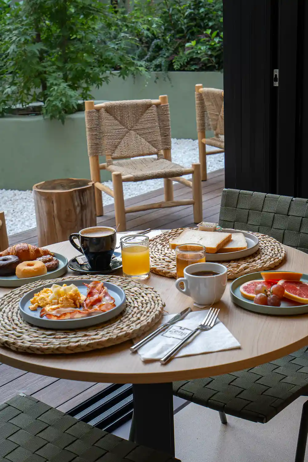 Mesa del patio con huevos revueltos, bacon, tostadas, fruta, café y zumo de naranja