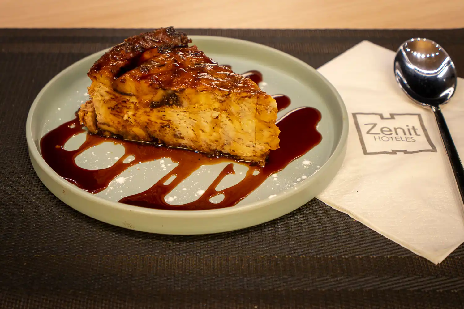 Porción de tarta casera bañada en salsa de caramelo, con una cuchara sobre la servilleta